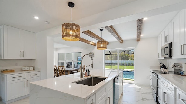Una cocina moderna con armarios blancos, una isla grande con pileta y vista a un patio con piscina.