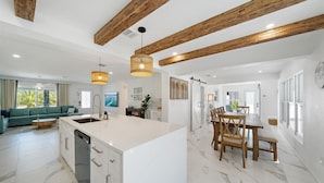 Una cocina amplia con una isla grande, vigas de madera en el techo y un comedor con mesa y sillas de madera.