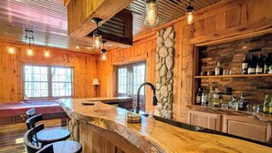 A rustic wooden bar area with a stone accent wall, bar stools, and a variety of bottles on shelves.