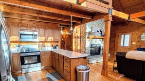 A spacious kitchen with wooden cabinets, a central island, stainless steel appliances, and a stone fireplace.