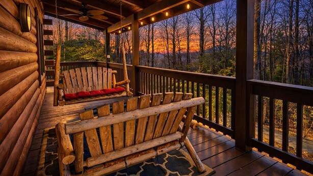 A log cabin with a porch featuring two wooden benches and a ceiling fan.
