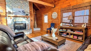 A cozy cabin interior with a stone fireplace, leather furniture, and a bookshelf.