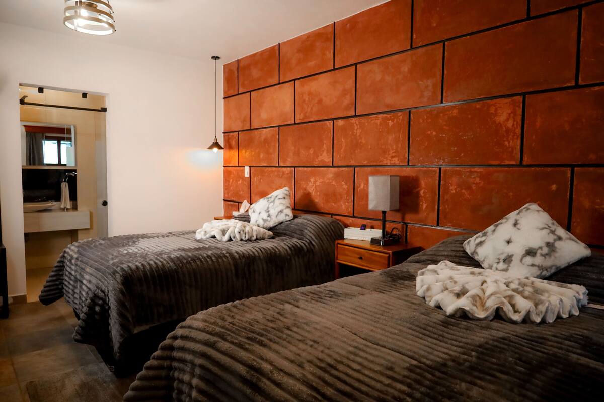 Ein Hotelzimmer mit zwei Betten, einem Ziegelstein-Muster-Kopfschild, einem Nachttisch mit Lampe und einem Spiegel.