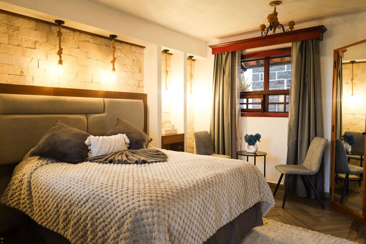 Ein Schlafzimmer mit einem großen Bett, einer Steinwand, einem Holz-Kopfteil, einem kleinen Tisch mit einer Vase und einem Stuhl.
