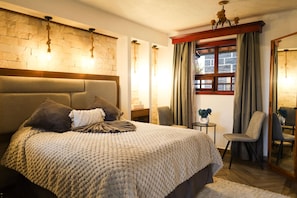 Une chambre avec un grand lit, un mur en pierre, une tête de lit en bois, une petite table avec un vase et une chaise.