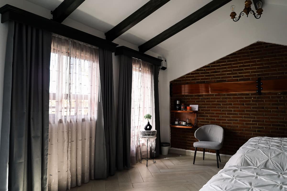 Ein Zimmer mit einem Bett, einem Sessel, einem kleinen Tisch mit Pflanze und einer Backsteinwand.
