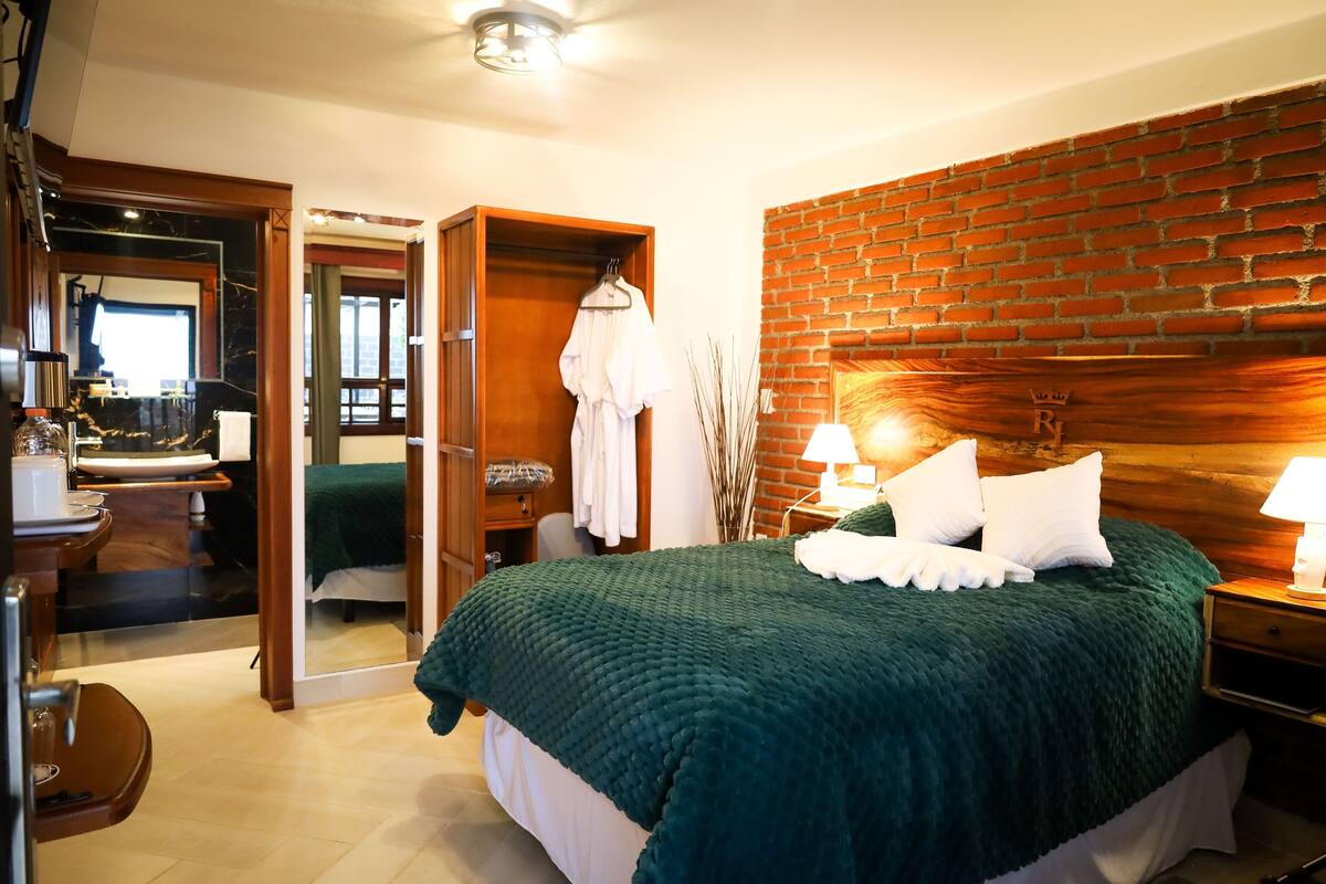 Ein Hotelzimmer mit einem Bett, einem Holzschrank, einem Schreibtisch mit Stuhl, einem Spiegel und einer Backsteinwand.