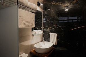 A modern bathroom with a large white sink, a glass shelf with toiletries, and a towel rack with a white towel. - Hotel Royal Inglés (Mineral del Monte)