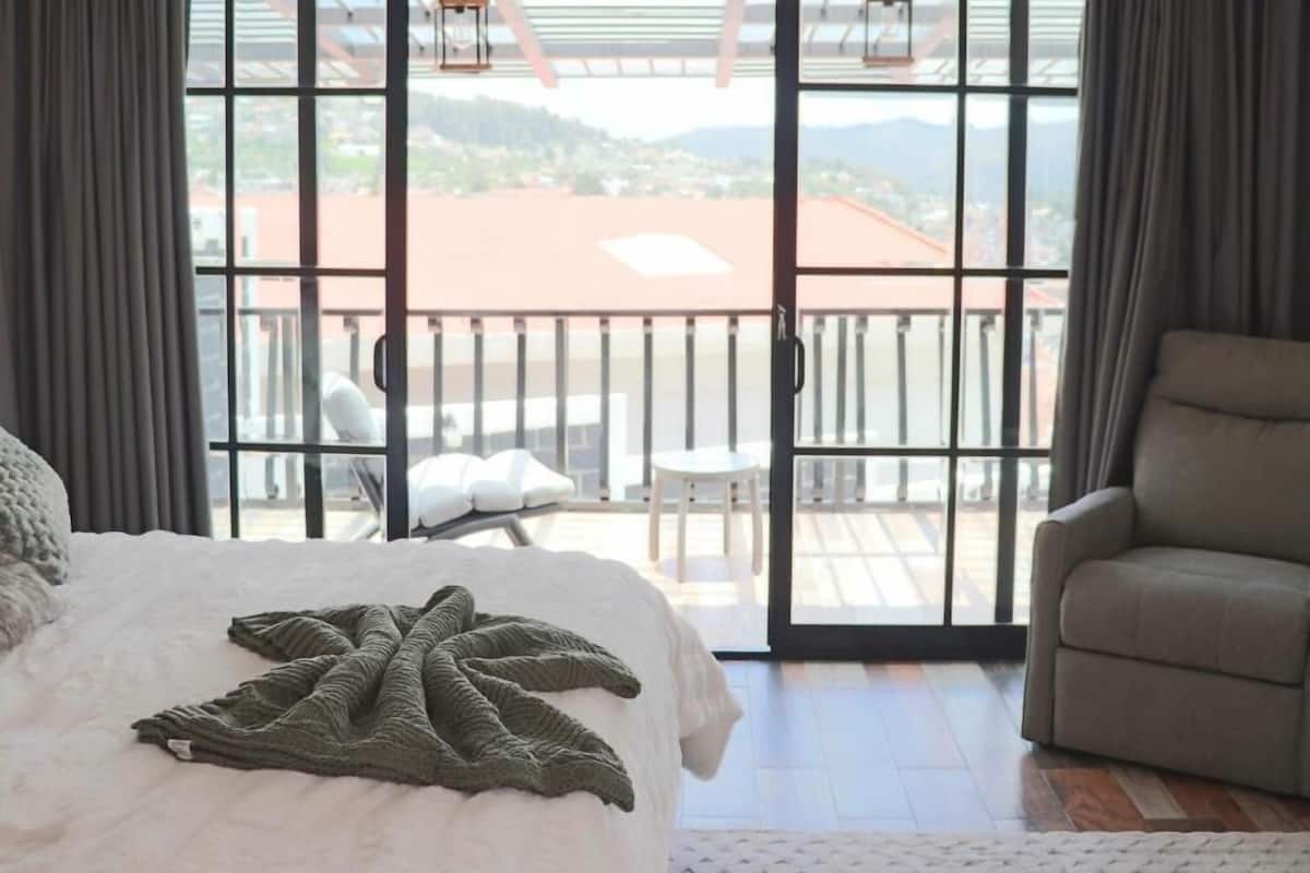 Ein Schlafzimmer mit einem großen Bett, Blick auf einen Balkon mit Stühlen und Blick auf ein Gebäude mit rotem Dach.