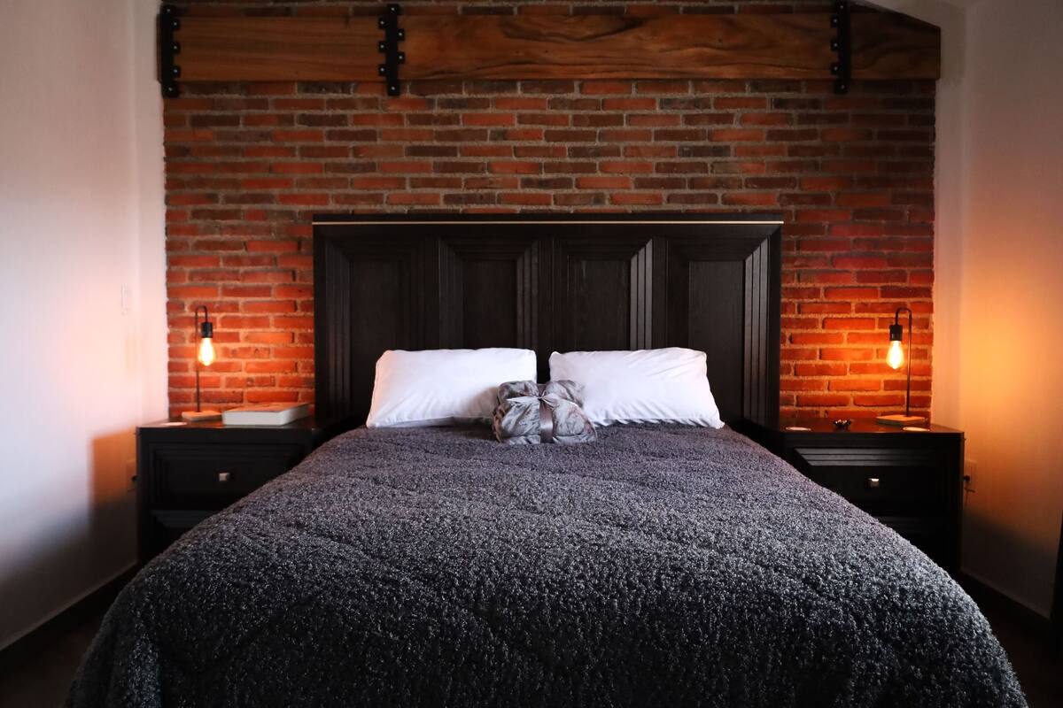 Ein Bett mit dunkelbrauner Kopfteil, zwei weiße Kissen und eine graue Decke.