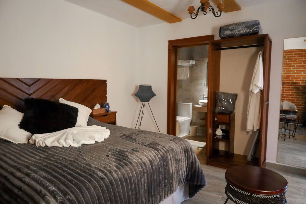 Ein Schlafzimmer mit einem großen Bett, einem Holzkopfteil, einem Nachttisch, einer Lampe und einem Spiegel.