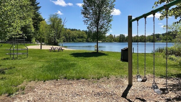 A park with a swing set, picnic table, and a bench near a lake. - Pristine 3 Bedroom, Walk-to Gt Barrington Center! (Great Barrington)
