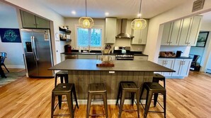 Una cucina moderna con isola centrale, sgabelli da bar, elettrodomestici in acciaio inossidabile e illuminazione a sospensione.