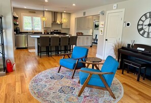 A modern kitchen with bar stools, a dining area with blue chairs, and a piano. - 5 Stars w/ Hot Tub, Sunny Patio, Game Room, Views! (Great Barrington)