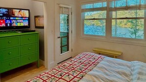 A bedroom with a bed, a green dresser, a television, and a window with a view of trees. - Direct on Lake Garfield: Book Fall Weekends! (Monterey)