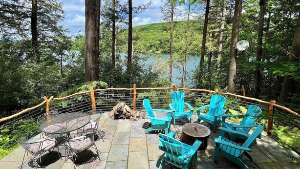 A deck with outdoor seating, a fire pit, and a view of a lake surrounded by trees. - Direct on Lake Garfield: Book Fall Weekends! (Monterey)