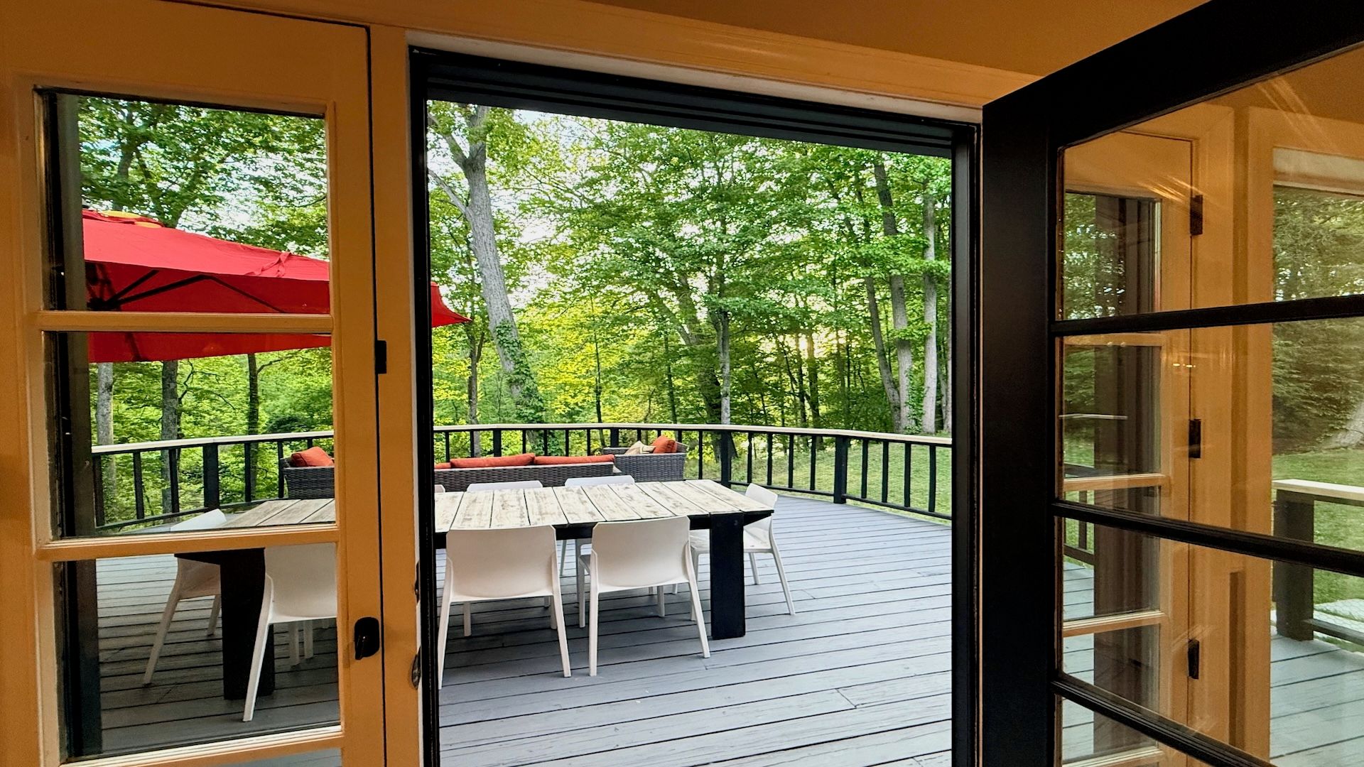 An open deck with a table and chairs, surrounded by a wooden railing, and a view of a forested area.
