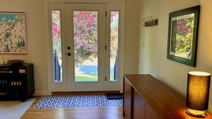 A wooden-floored entrance with a glass door leading outside, a patterned mat, a wooden bench, and a wall-mounted lamp. - Chic, Mid Century 3+ Bedroom with Hot Tub! (Great Barrington)