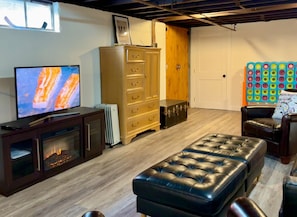 Ein Zimmer mit Fernseher, Schrank, Kommode, Hocker, Stuhl und Wandregal.