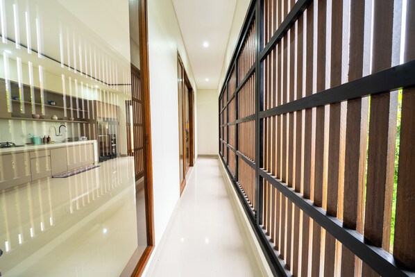 A hallway with a reflective floor, a kitchen area with cabinets and appliances, and a wooden partition with vertical slats.