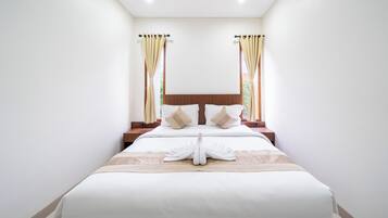 A neatly made bed with a white duvet and a towel arranged in a swan shape, a wooden headboard, and curtains on the windows.