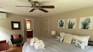 A bedroom with a large bed, a ceiling fan, a chair, and a door leading to another room.