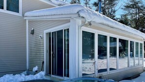 A house with a covered hot tub and a sliding glass door leading to a snowy yard.