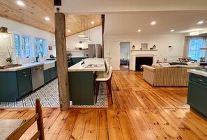 A spacious kitchen with wooden flooring, a central island, and a dining area with a sofa. - Light-filled, Stylish, Farmhouse Colonial, Egremont MA (Egremont)