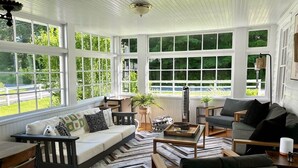 Ein sonnendurchflutetes Zimmer mit großem Fenster, einer Couch, einem Couchtisch und einem Sessel.