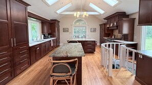 Una cocina con alacenas de madera oscura, una isla central con encimera de mármol y un comedor con una silla.