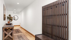 Un pasillo con un banco de madera, una mesita con un cuenco y una planta, y un espejo decorativo en la pared.