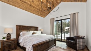 Un dormitorio con techo de madera, una cama grande, una mesita de noche, una silla y vistas al exterior a través de una ventana.