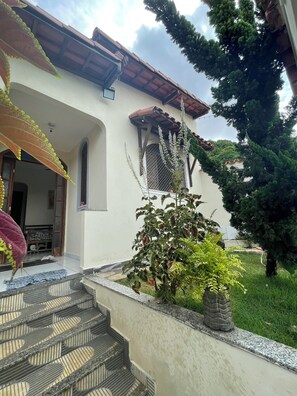 A house with a tiled roof, a small garden with steps leading to the entrance, and a window with a metal grill. - Pet-Friendly Home (Guarapari)