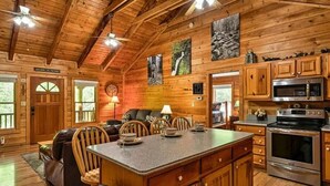 Ein Blockhaus-Interieur mit Holzausstattung, einem Essbereich mit Tisch und Stühlen, einer Küche mit modernen Geräten und einem Kamin.