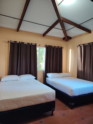 Two beds with white linens, a window with curtains, and a tiled floor.