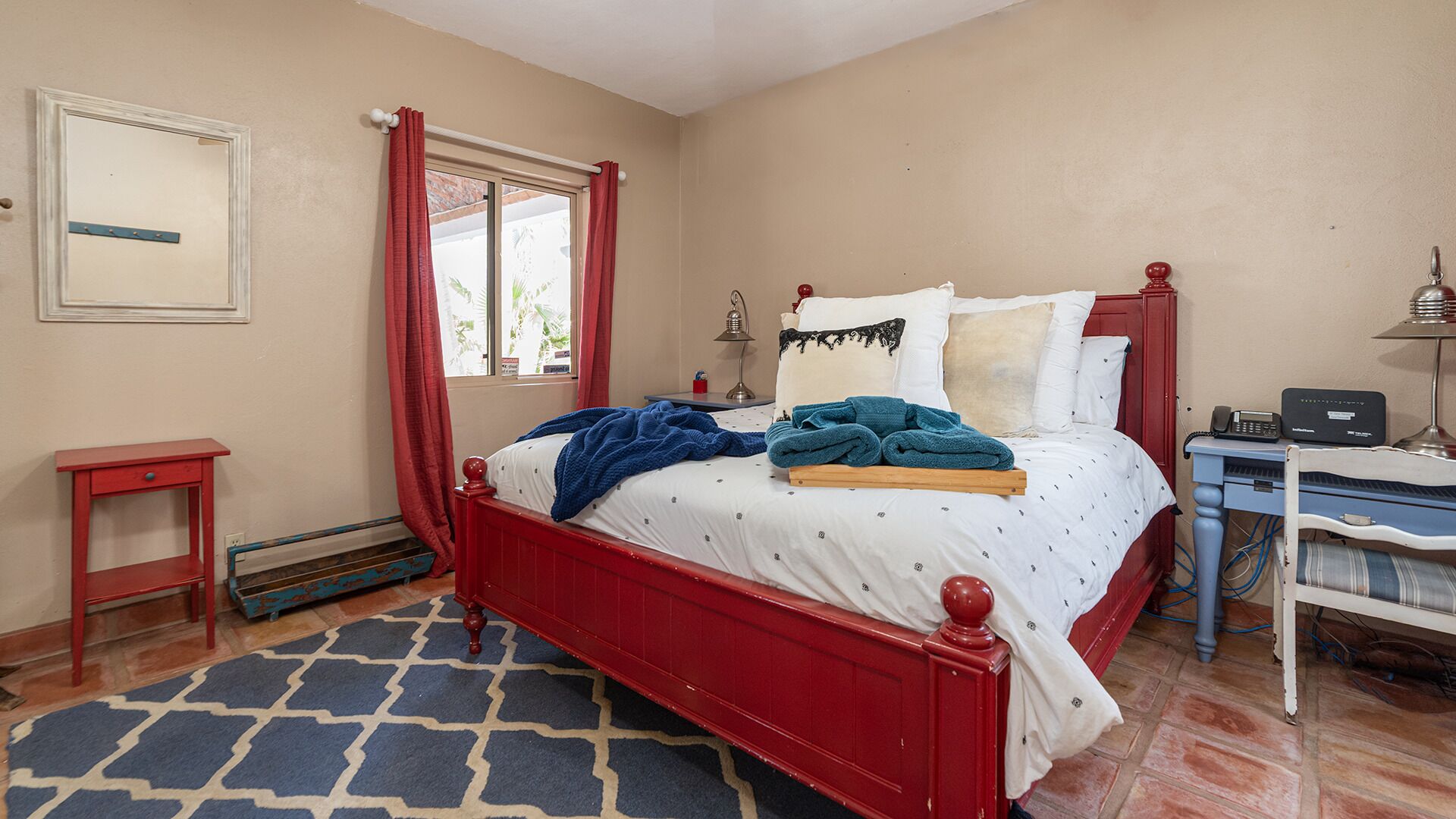 Quarto com cama de dossel, mesa de cabeceira pequena, criado-mudo, abajur e telefone.