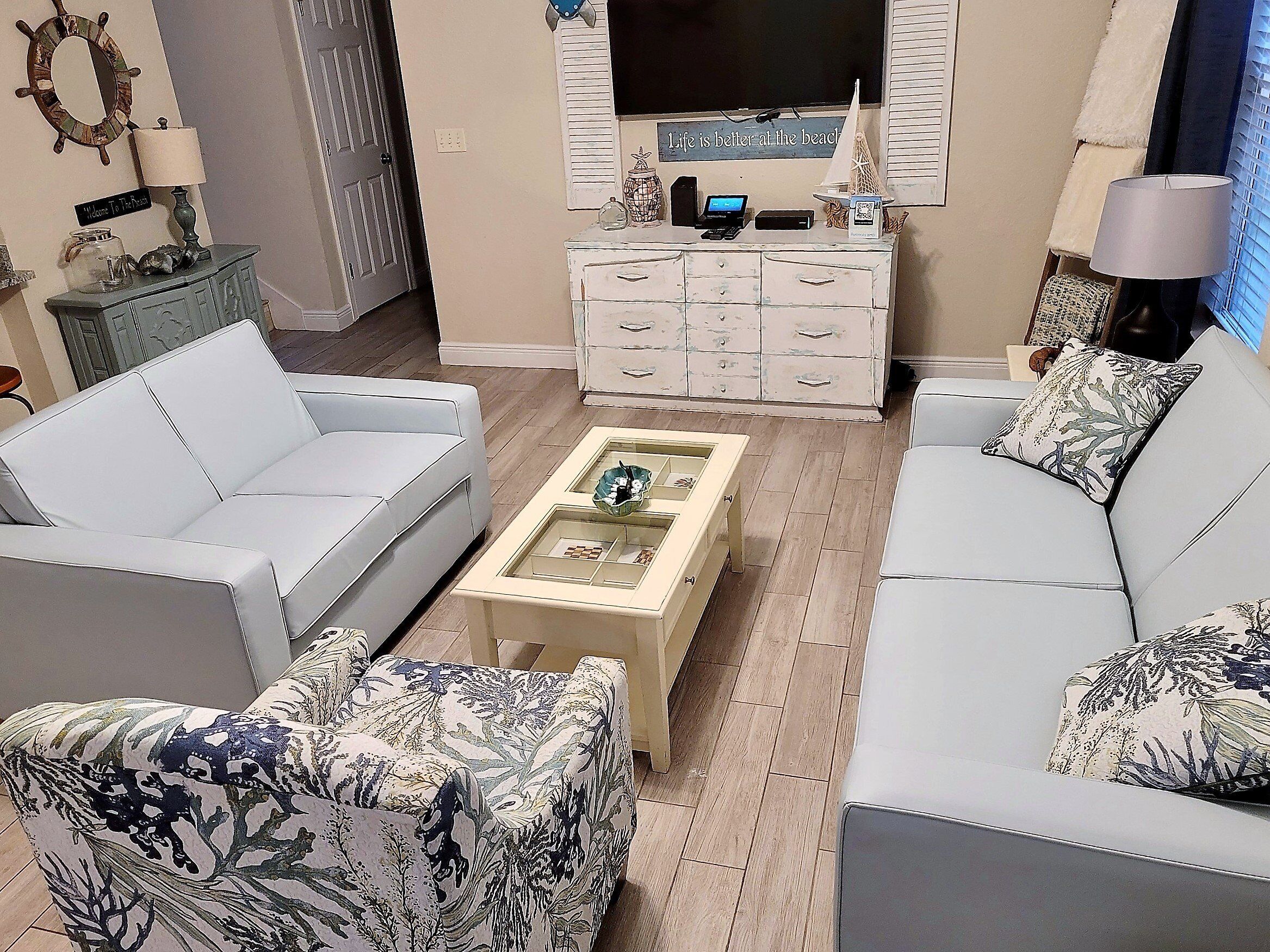 A living room with a white sofa, a patterned armchair, a coffee table, and a TV on a stand.