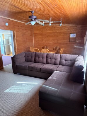 Een gezellige kamer met een hoekbank, houten plafond en een plafondventilator.