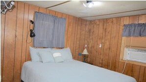 A bedroom with a wooden paneled wall, a bed with white bedding, a lamp, and a window with a curtain. - Property Rental 699 Per Week + Boat Rental 799 Per Week + Fees (Barnett)
