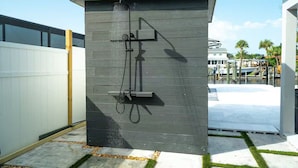 Una ducha exterior moderna con diseño de panel de madera, ubicada en una zona residencial con vista a un puerto deportivo y barcos.