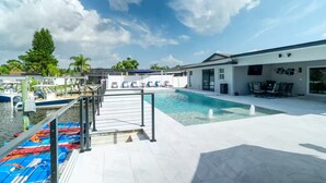 Un área de piscina moderna con vistas despejadas al agua, una terraza con sillas de descanso y un edificio con zona de comedor.