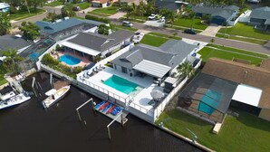 Vista aérea de una propiedad frente al mar, con piscina, barcos amarrados y una zona exterior cubierta.