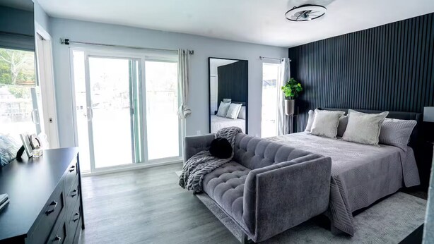 Un dormitorio moderno con una cama grande, un sofá gris y un aparador.