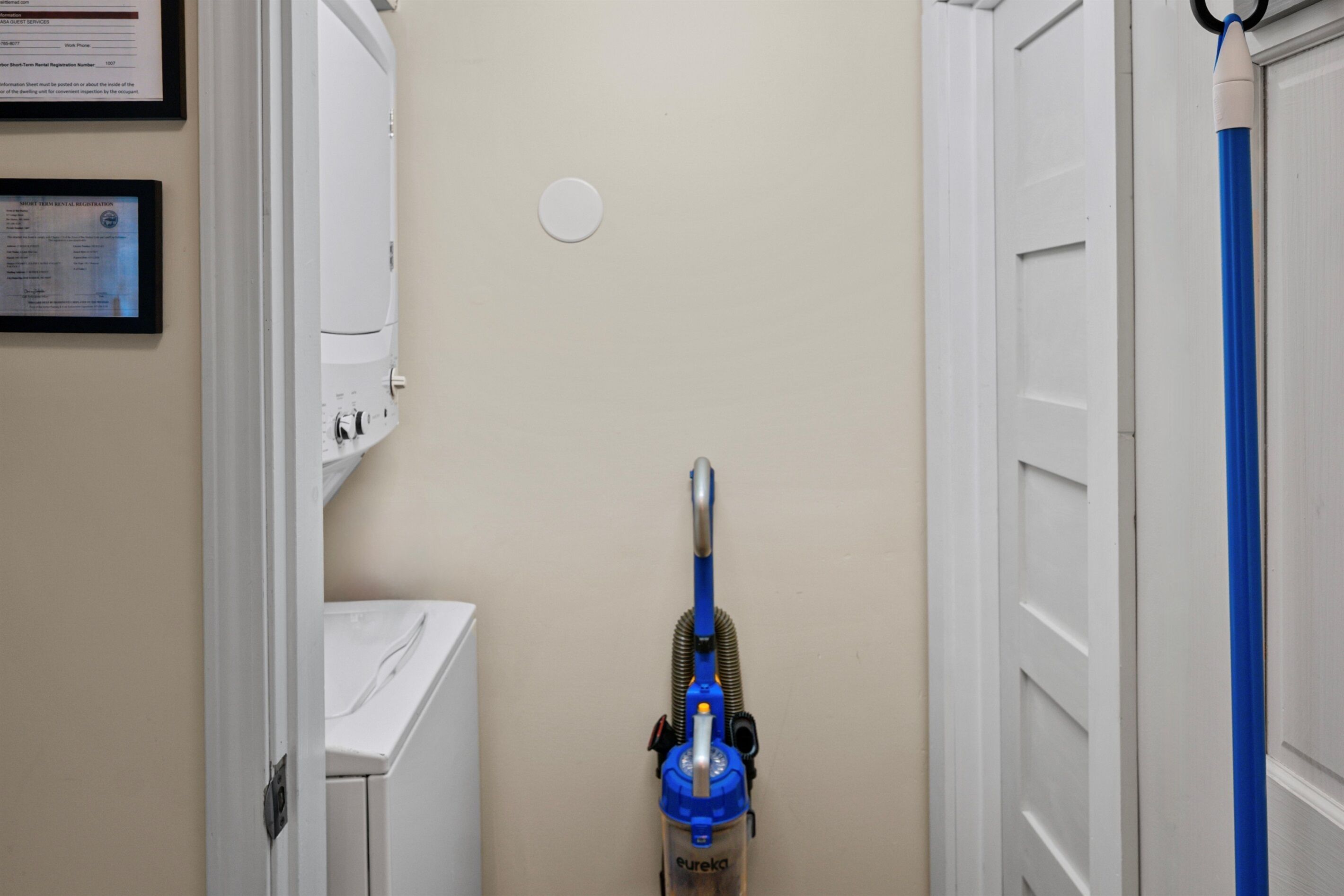 A narrow hallway with a white door on the right, a blue vacuum cleaner in the center, and a white appliance on the left.