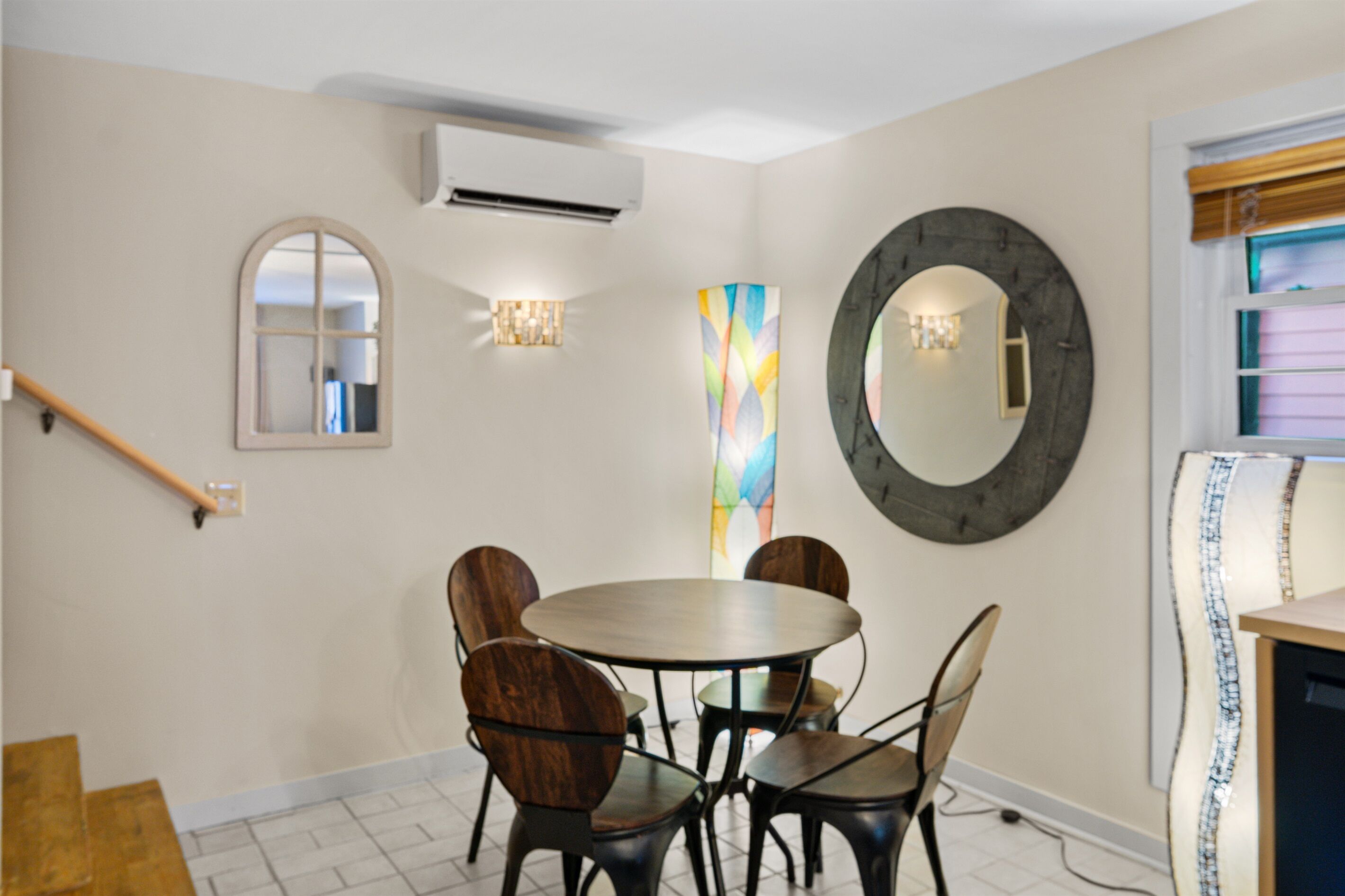 A dining area with a round table and chairs, a large mirror, and a colorful abstract painting on the wall.