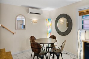 Un coin repas avec une table ronde et des chaises, un grand miroir et un tableau abstrait aux couleurs vives accroché au mur.