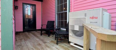A pink house with a wooden deck, two black chairs, and a white air conditioning unit.