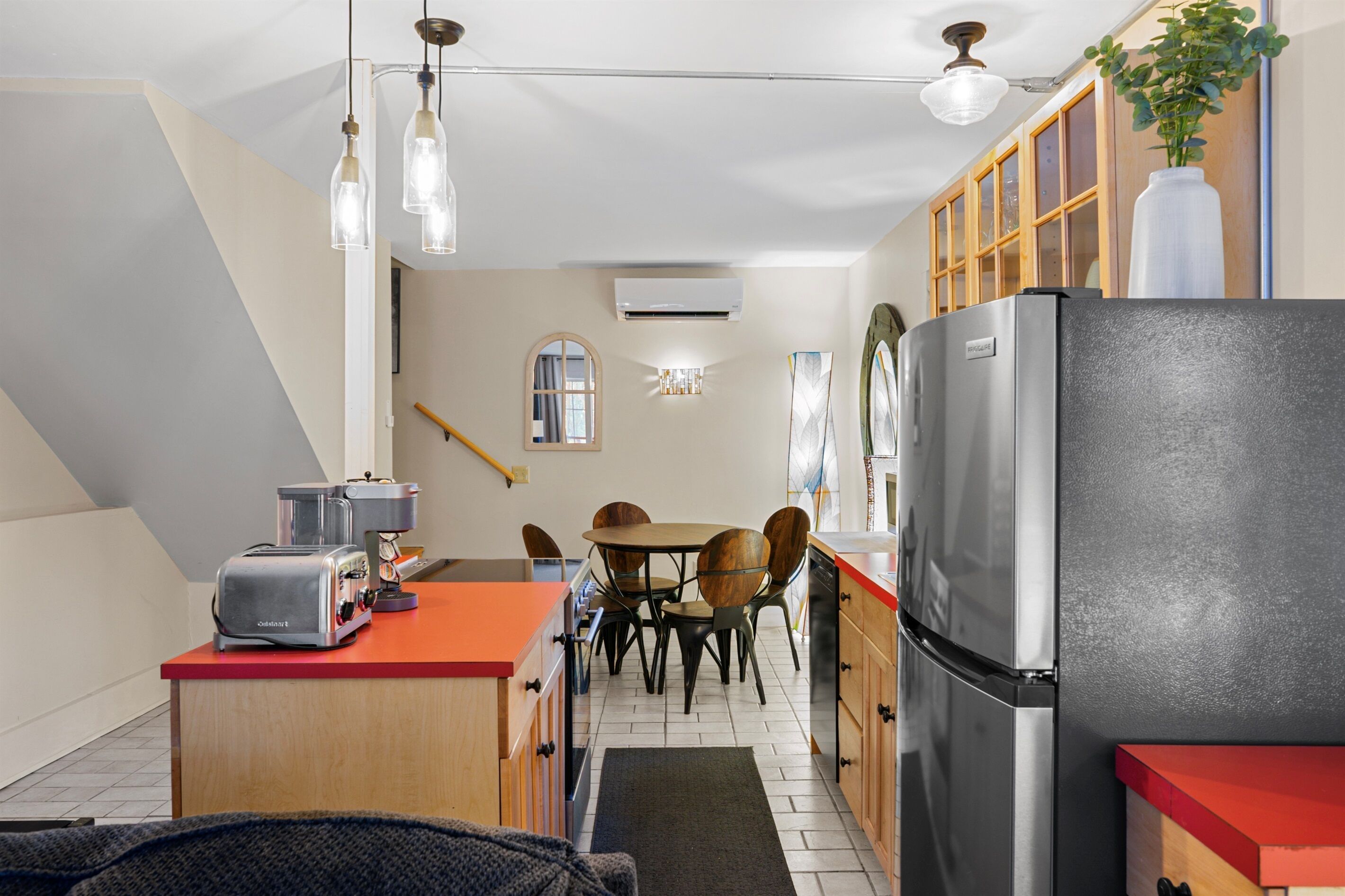Una cocina compacta equipada con refrigerador, tostadora y una mesa de comedor de madera con sillas.