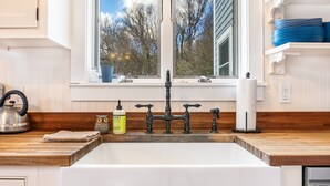 A kitchen with a white sink, wooden countertop, and a window with a view of trees. - Acadia View Cottage: Peaceful, Pet Friendly, Fire Pit, Near Peaks and Echo Lake (Mount Desert)