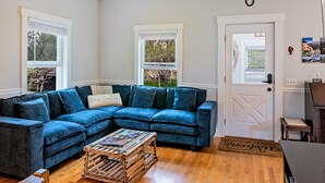 A living room with a blue sectional sofa, a wooden coffee table, and a door with a white frame. - Acadia View Cottage: Peaceful, Pet Friendly, Fire Pit, Near Peaks and Echo Lake (Mount Desert)